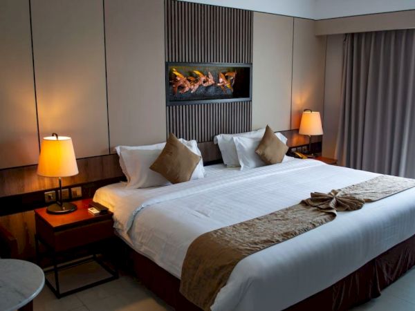 A hotel room with a large bed, two bedside lamps, decorative pillows, and curtains. A wall decor piece is above the bed.