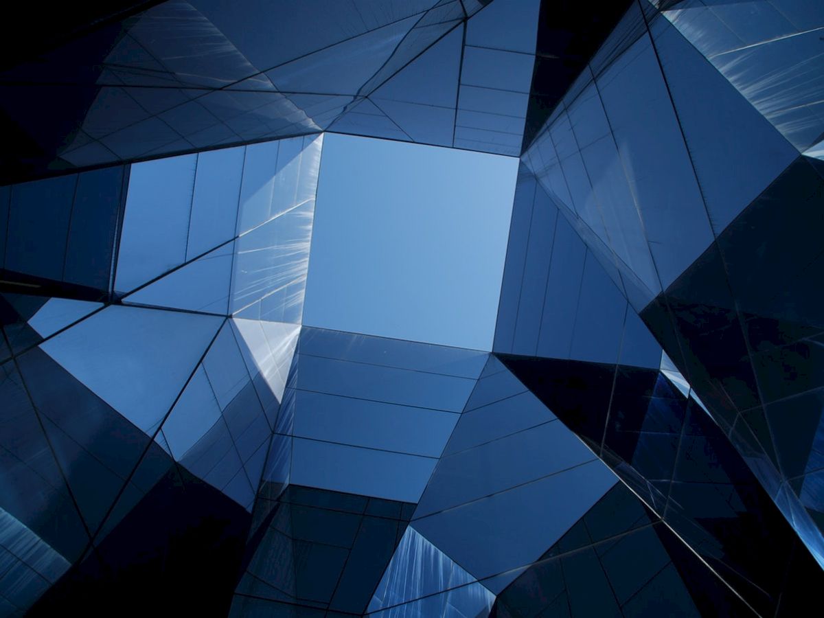 Geometric glass structures form a grid pattern, reflecting light and sky, creating a modern architectural design.