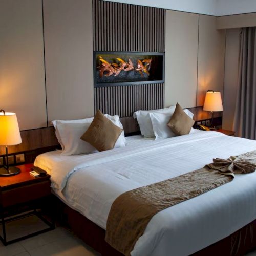 A neatly made hotel room features a large bed with pillows, bedside lamps, and folded towels, under stylish wall decor and soft lighting.
