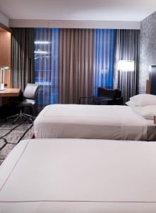A modern hotel room with two beds, a flat-screen TV, desk, and stylish decor.