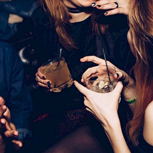 People enjoying a night out, holding drinks and laughing, captured in a lively social setting.