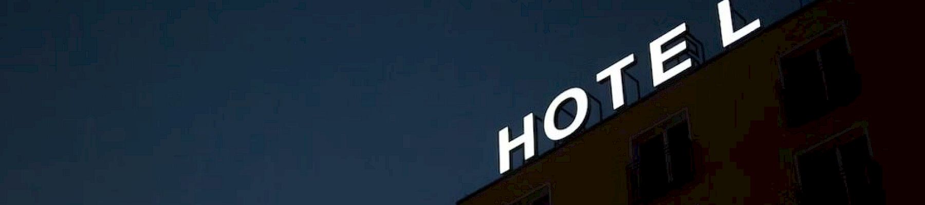 A building with a "HOTEL" sign missing the letter "T" against a dark evening sky.