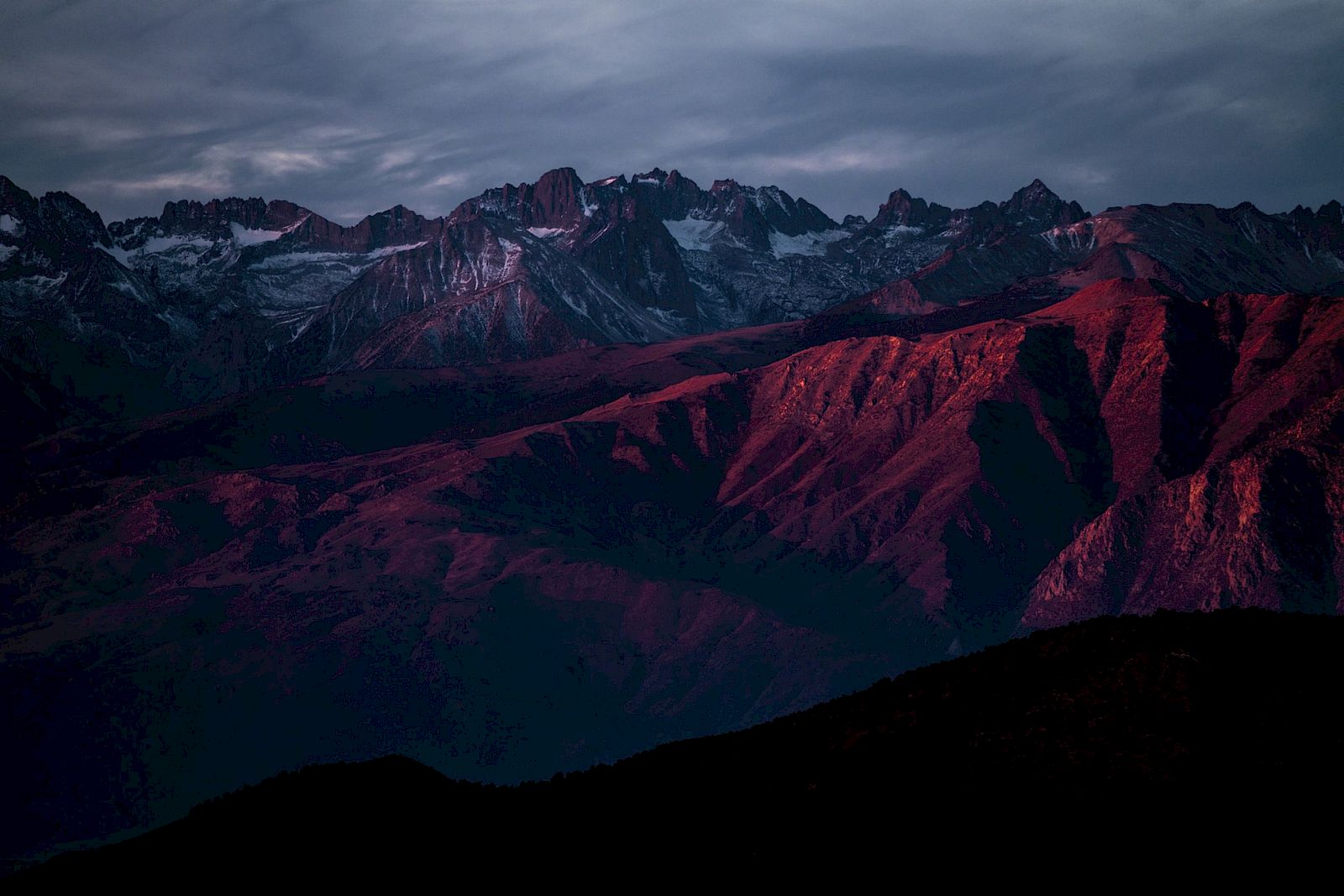A mountain range bathed in red and purple hues under a dark, cloudy sky.