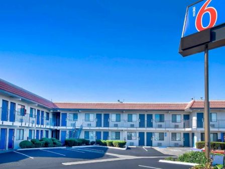 The image shows a two-story motel building with a "6" sign, a parking lot, and a clear blue sky in the background.