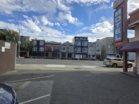 A motel parking lot with a "VACANCY" sign, surrounded by buildings under a partly cloudy sky.