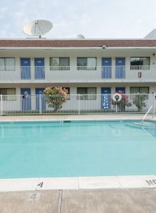The image shows a hotel pool area with a two-story building, lounge chairs, and a "No Diving" sign surrounding the pool.