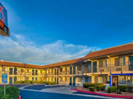 The image shows a motel with a "6" logo on the sign and building, featuring two stories, outdoor walkways, and a parking area.
