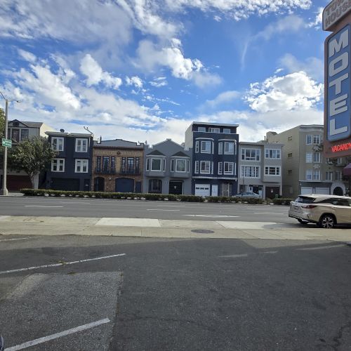 A parking lot with a "Motel" sign on the right, overlooking a street with colorful houses and a cloudy sky.