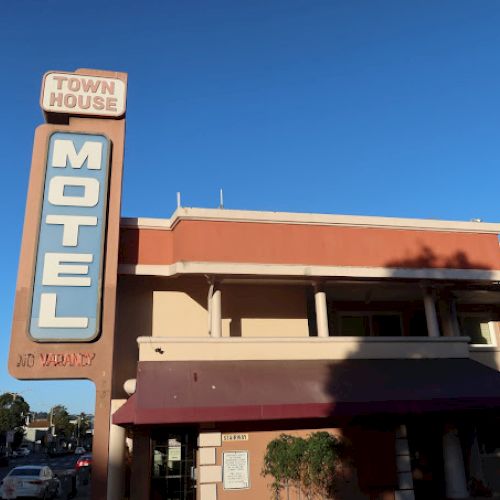 The image shows a building with a sign reading "Town House Motel" under a clear blue sky, featuring a shadow on the facade.