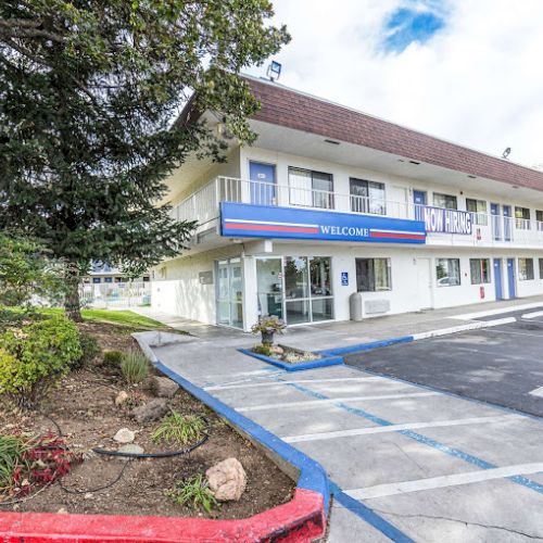 A two-story motel building with a "Welcome" sign, parking spaces, and landscaped greenery around the area.
