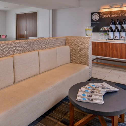 The image shows a cozy coffee area with a beige couch, a table with newspapers, and a coffee counter labeled "Smart Roast Coffee."