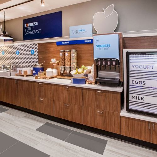A breakfast buffet with cereal dispensers, yogurt, eggs, and milk fridge, and a juice section labeled "Squeeze the Day."