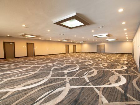 Spacious, empty room with patterned carpet, recessed lighting, and doors along the walls, suitable for events or gatherings.