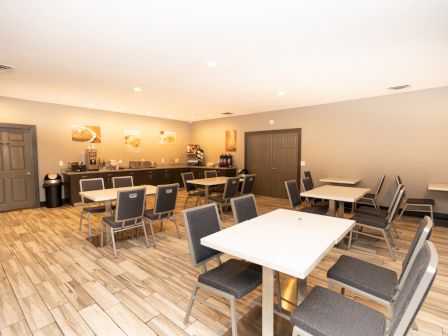 A clean dining area with tables, chairs, and a beverage counter in the corner, featuring a bright and neutral color scheme.
