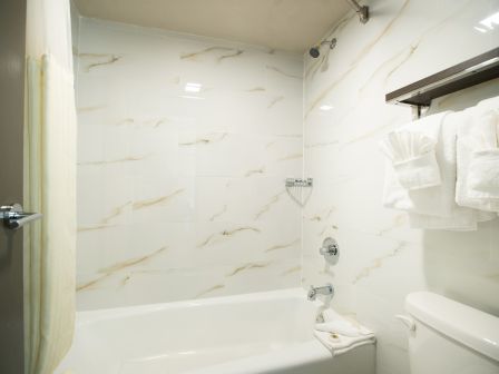 A bathroom with a bathtub, shower curtain, towel rack with folded towels, and toilet. The walls have a marble-like pattern.