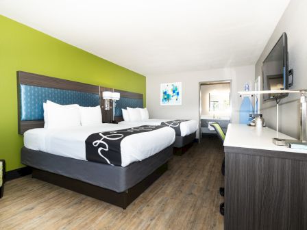 A hotel room with two double beds, a TV mounted on the wall, and modern furnishings in a bright, welcoming setting.