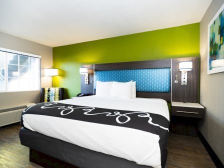 A modern hotel room with a large bed, bright green accent wall, bedside tables, lamps, window, and wall art in a cozy setting.