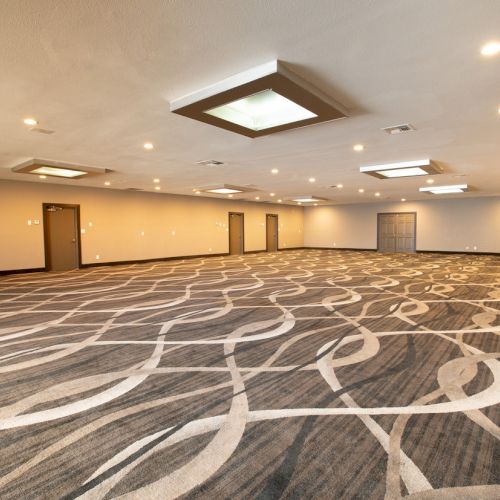 An empty, spacious conference room with patterned carpet, recessed lighting, and several closed doors, ideal for events or meetings.