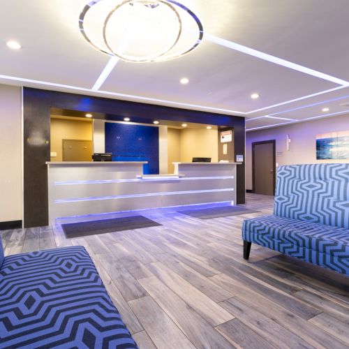 The image shows a modern hotel lobby with patterned seating, a reception desk, wooden flooring, and ambient lighting.
