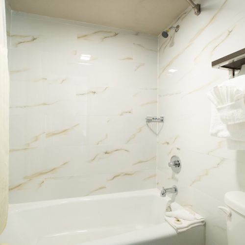 A clean bathroom with a white bathtub, marble walls, a towel rack with folded towels, and a closed door to the left.