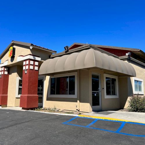 A small building with beige walls, red accents, and an awning, set against a clear blue sky. There are parking spaces in front.