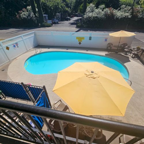 A small outdoor pool with yellow umbrellas, lounge chairs, and a white fence, set in a sunny area.