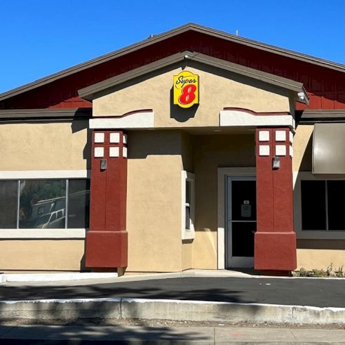 The image shows a building with a Super 8 logo on the front, featuring tan walls and red accents under a clear blue sky.