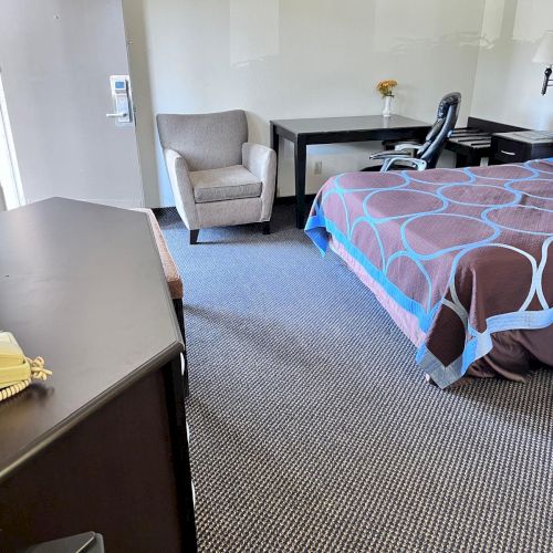 A hotel room with a bed, desk, chair, TV, and phone. The decor is simple, and the room looks clean and organized.