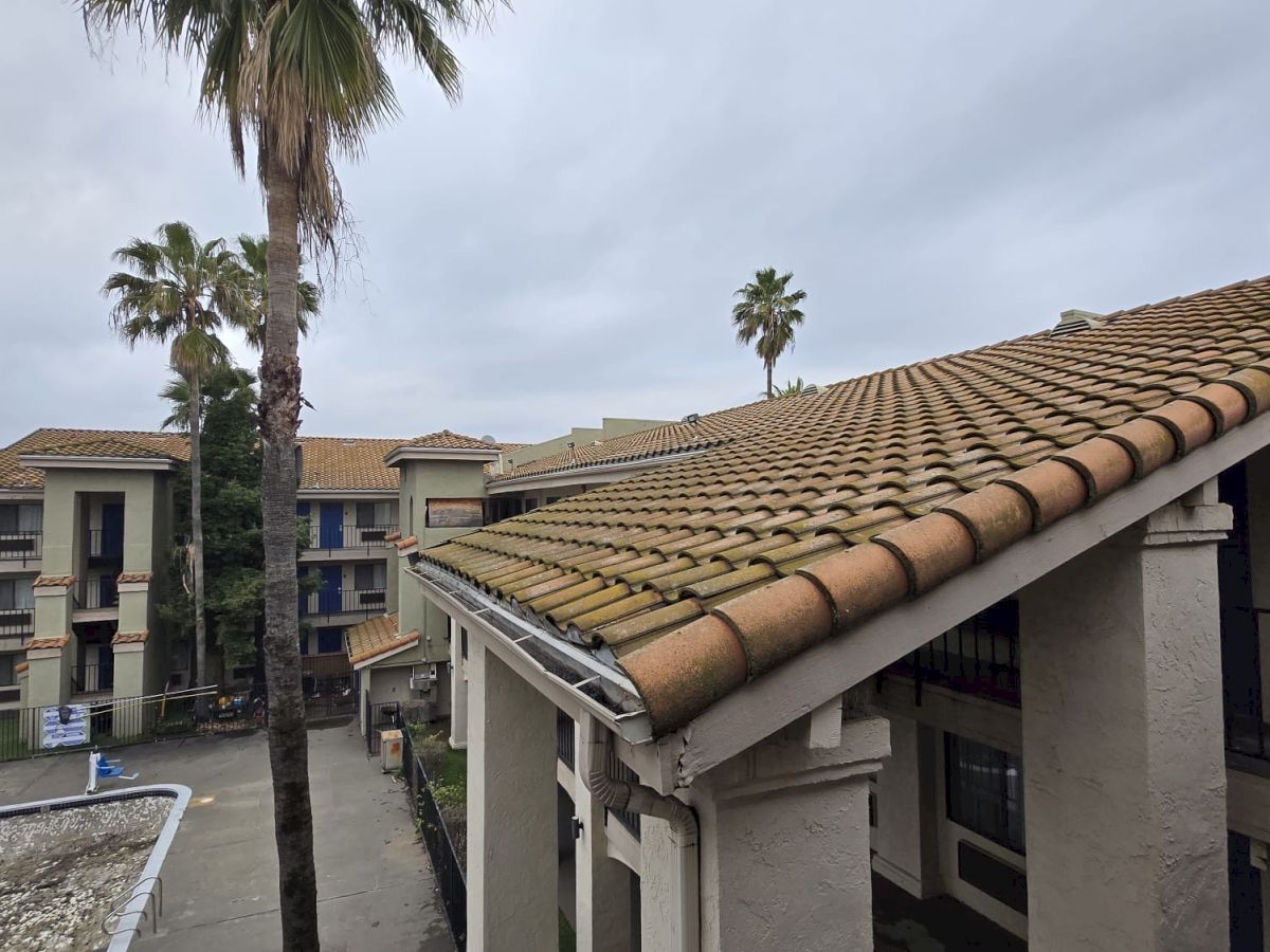 A view of buildings with tiled roofs and palm trees on a cloudy day, featuring balconies and walkways in a residential area.