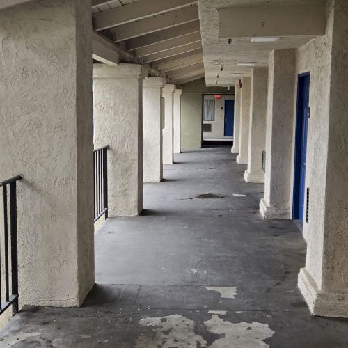 A covered outdoor corridor with a sloped ceiling, concrete floor, and blue doors along the wall, possibly part of a motel or apartment complex.