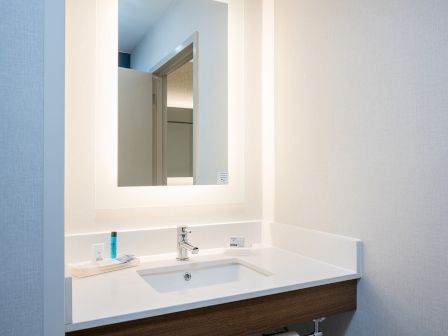 A modern bathroom vanity with a white countertop, integrated sink, wood cabinet, and a backlit rectangular mirror.