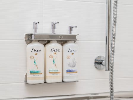 Three Dove shampoo/conditioner bottles on a wall-mounted rack in a bathroom shower.