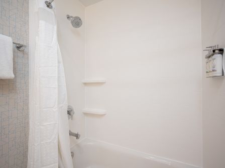 A white bathroom shower with a curtain, built-in shelves, a towel hanging on a hook, and a clean, minimal look.