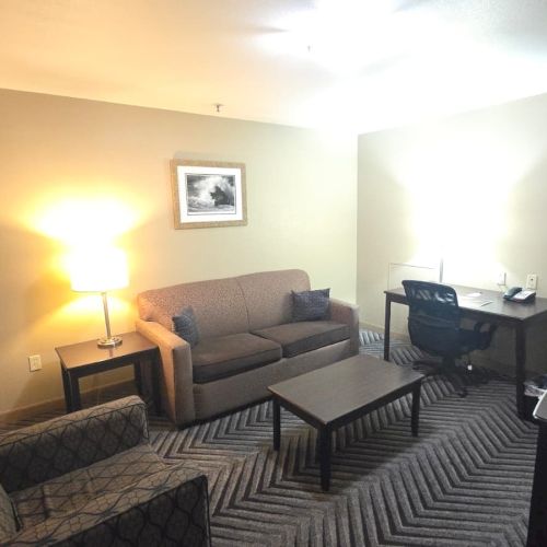 A hotel-style lounge with two sofas, a coffee table, an office desk setup, shelves, and framed wall art.