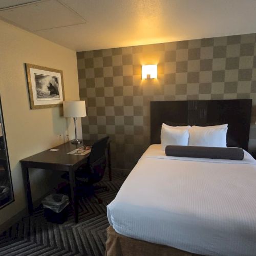 A neat hotel room with a king bed, checkered accent wall, desk, lamps, and framed art.