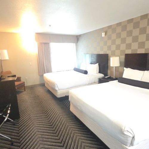 A modern hotel room with two neatly made beds, lamps, a TV, and a checkerboard accent wall.