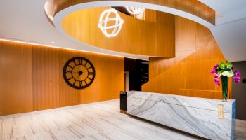 A modern lobby with wood accents, a large clock, marble reception desk, and contemporary lighting fixtures.