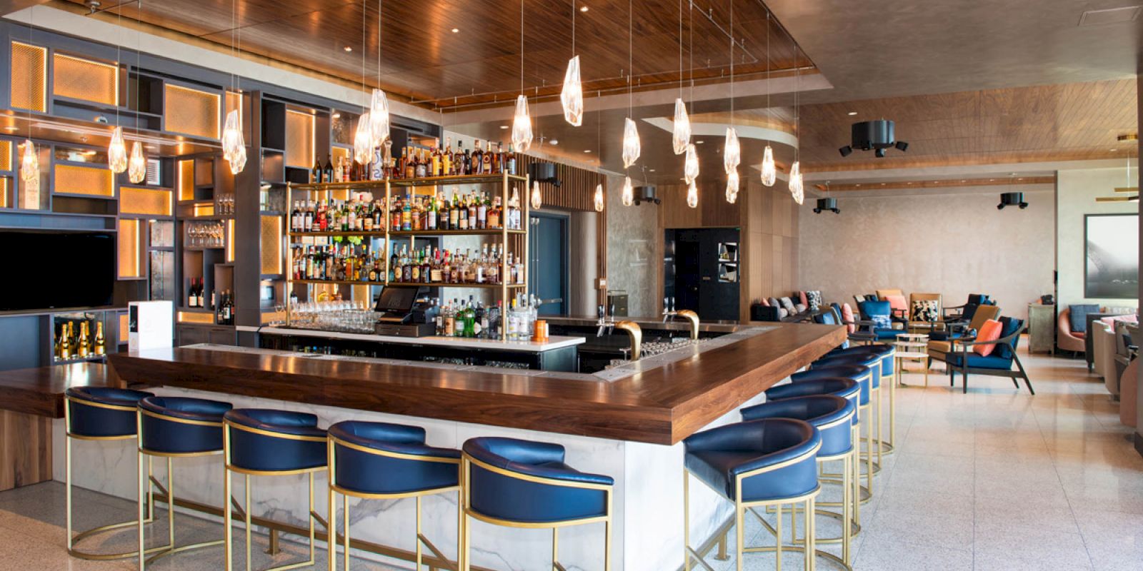 A modern bar with a stocked counter, stylish barstools, pendant lights, and a seating area. Cozy and inviting ambiance.