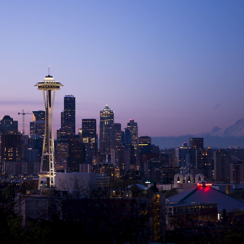 Seattle skyline at dusk, featuring the Space Needle and cityscape with Mount Rainier visible in the background.