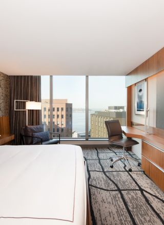A modern hotel room with a large bed, work desk, chair, flat-screen TV, and a city view from the window completes the cozy setup.