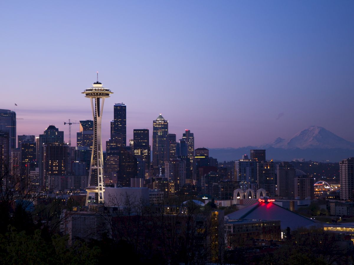 Seattle skyline at dusk, featuring the Space Needle and city skyscrapers, with Mount Rainier visible in the background.