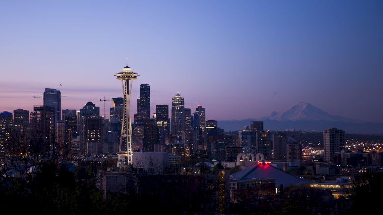 Seattle skyline at dusk, featuring the Space Needle and city skyscrapers, with Mount Rainier visible in the background.